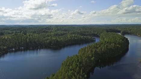 Aerial-footage-of-a-Finnish-lake-in-summer,-blue-sky,-heavy-clouds-and-sun,-long-island