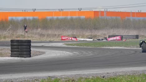 Slow-motion-shot-of-a-drifting-green-car-on-a-race-track-with-a-pile-of-tires-and-s-turn