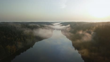 Beautiful-foggy-lake-aerial-shot-through-clouds-at-sunrise,-revealing-shot,-establishing-nordic-climate-and-nature