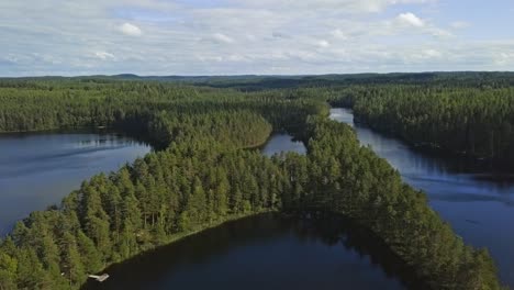 Aerial-footage-of-a-Finnish-lake-in-summer,-blue-sky,-heavy-clouds-and-sun,-x-shape-island