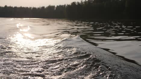 Big-wave-on-a-lake-while-in-a-boat-with-sun-shining-in-the-background-blurry-forest-moody-evening-atmoshere