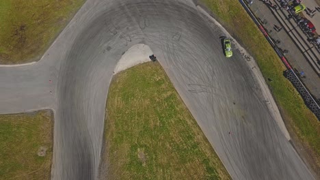 Aerial-shot-of-a-car-drifring-on-high-speed-on-a-turn,-green-grass-and-a-race-track,-top-view-shot,-next-to-viewers