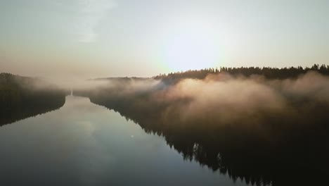 Beautiful-foggy-lake-aerial-shot-through-clouds-at-sunrise