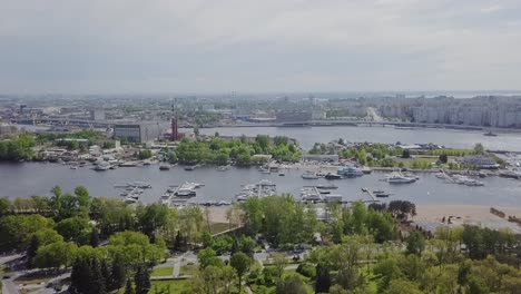 Port-part-of-the-city-with-many-ships,-yachts,-factory-in-the-background,-city-panorama,-industrial-green-park-and-trees