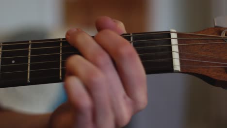 A-close-up-of-a-young-man-is-playing-guitar,-the-camera-pans-left-to-show-his-strumming-hand