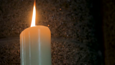 White-candle-burning-on-dark-stone-wall-background-in-church