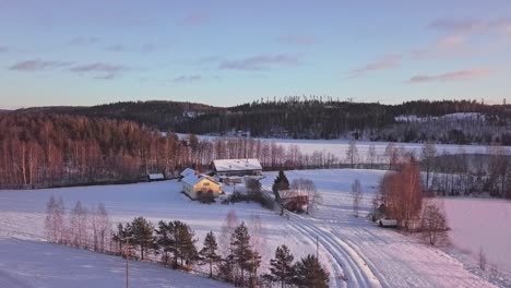 Aerial-rural-landscape-of-winter-house-next-to-a-frozen-lake-and-sun