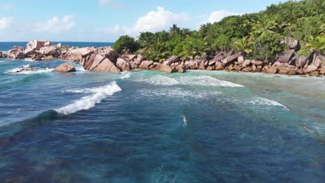 Aerial-view-following-the-waves-rolling-towards-the-unpeopled,-white-beaches-at-Anse-Coco,-Petit-Anse-and-Grand-Anse-on-La-Digue,-an-island-of-the-Seychelles