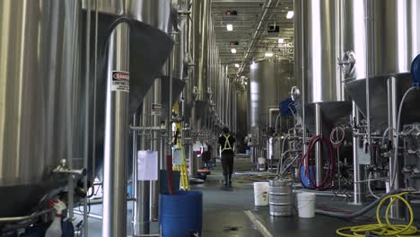 Brewery-worker-walking-through-large-line-of-brew-kettles