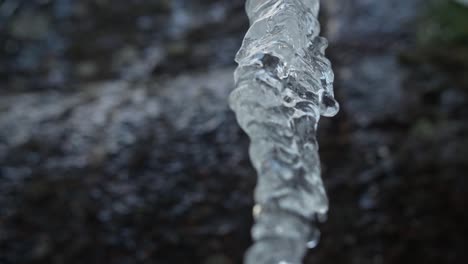 Ice-icicle-over-a-blurry-background-and-rocky-mountain-in-winter-forest