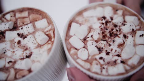 Two-cups-of-cacao-in-warming-up-hands-of-people-with-marshmallow-in-winter-with-snow-in-the-background
