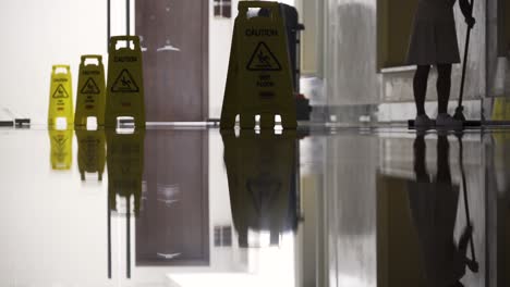 Maid-cleaning-shiny-floor-with-multiple-caution-signs