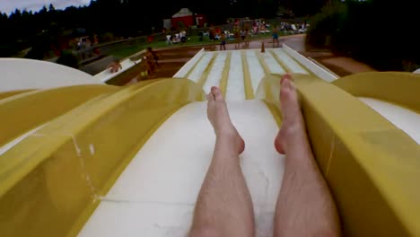 Young-man-sliding-down-a-yellow-water-slide-in-amusement-par,-public-bath-and-landing-in-a-splash-of-water,-unrecognizable,-legs-only