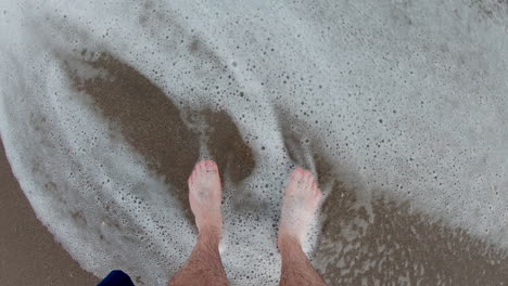 Man's-feet-in-the-sand,-standing-along-the-edge-of-the-surf