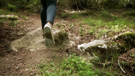 Fit-woman-in-black-thights-wearing-light-sneakers-hiking-on-rocky-dirt-path-through-trees-of-forest-up-a-mountain