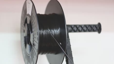 A-Spool-of-black-3D-printer-filament-sits-on-the-3D-Printer-spool-holder-and-winds-down-while-its-being-printed-with