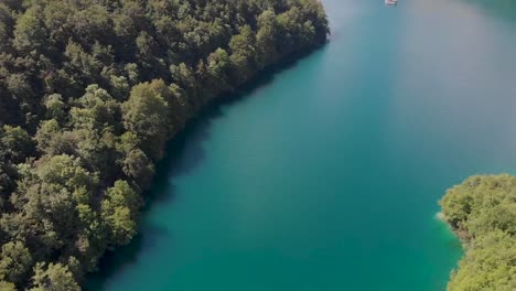 Panning-up-drone-shot-of-a-vivid-blue-lake-with-a-white-boat