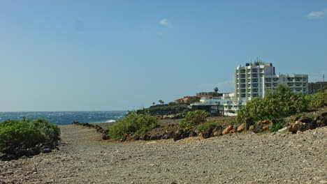 Tenerife-beach-road-with-a-hotel-and-waves-in-the-background-and-rocky-trail,-road