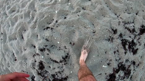 Man's-bare-feet-walking-along-sandy-beach-on-a-cloudy-day