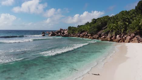 Aerial-view-following-the-waves-rolling-towards-the-unpeopled,-white-beaches-at-Anse-Coco,-Petit-Anse-and-Grand-Anse-on-La-Digue,-an-island-of-the-Seychelles