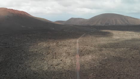 Ascending-and-turning-aerial-shot-of-a-barren-volcanic-field-with-a-dirt-road