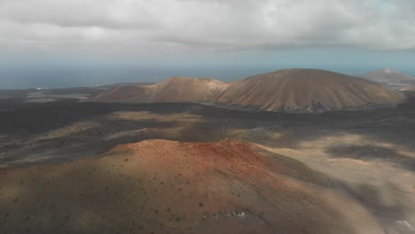 Pull-back-drone-shot-descending-behind-a-red-volcano-on-a-cloudy-day