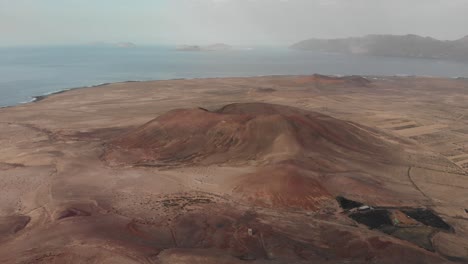 Pull-back-and-descending-drone-shot-behind-a-red-volcano-with-small-white-building-on-top