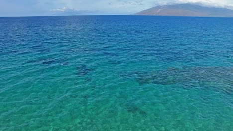 Panning-aerial-shot-over-clear-blue-water-in-Hawaii-with-land-in-background