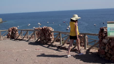 Young-woman-walking-towards-cliffside-lookout-point,-scenic-ocean-landscape,-Spain