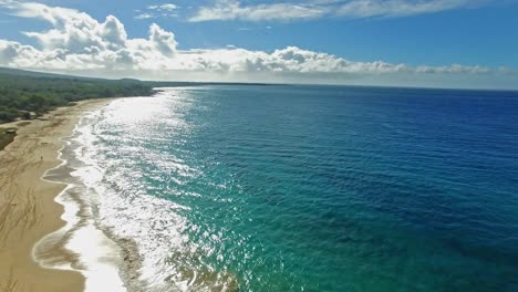 Panning-aerial-shot-into-the-sun-with-one-person-walking-on-on-the-coast-of-Maui-Hawaii-with-beautiful-blue-water-and-mountains