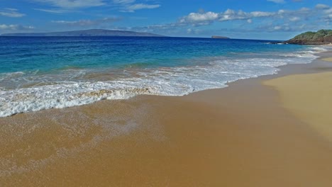 Waves-crashing-on-sandy-beach-in-Maui-Hawaii-with-beautiful-blue-sky-and-water