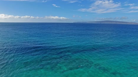 Panning-aerial-shot-of-a-snorkeler-in-Maui-Hawaii-in-beautiful-blue-water-with-land-in-the-background