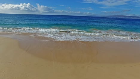 Panning-waves-crashing-on-sandy-beach-in-Maui-Hawaii-with-beautiful-sky-and-water