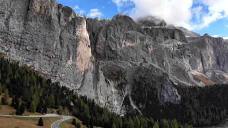 4K-drone-flying-up-near-dolomite-mountain-range-in-Italy-and-cars-driving-on-road