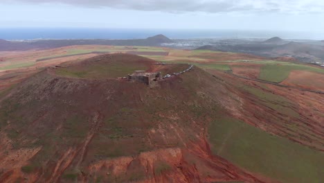 Pull-back-drone-shot-of-a-castle-on-a-rim-of-a-red-volcano
