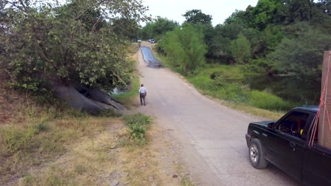 Foto-De-Un-Hombre-Caminando-Por-Un-Largo-Camino-En-El-Campo-Mientras-Una-Camioneta-Que-Transportaba-Electrodomésticos-Pasa-Junto-A-él