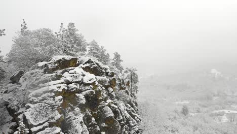 Aerial-view-of-drone-flying-past-a-rocky-outcropping-during-a-snow-storm