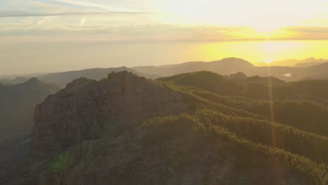 Beautiful-drone-shot-of-a-mountain-panorama-at-golden-hour-with-a-forest-and-lens-flare,-gran-canaria