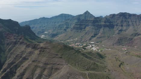 Drohnenaufnahme-Von-Bergen-Und-Schluchten-Mit-Einem-Kleinen-Dorf-Auf-Gran-Canaria