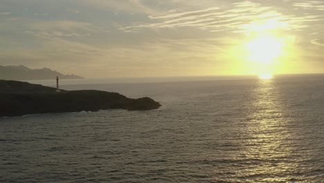 Drohnenaufnahme-Panorama-Eines-Leuchtturms-Zur-Goldenen-Stunde-Mit-Meer-Und-Sonne-Im-Hintergrund
