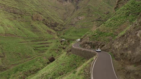 Drone-shot-of-a-car-driving-on-a-road-in-a-green-canyon
