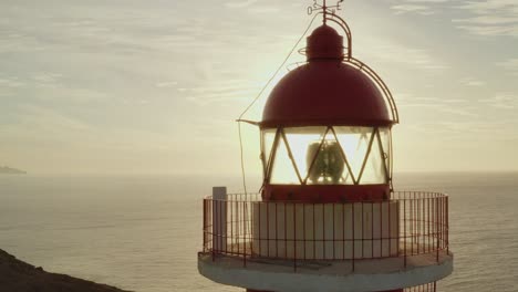 Close-up-drone-shot-of-a-lighthouse-with-sun-and-ocean-in-the-background-at-golden-hour