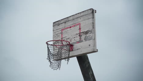 Alter-Basketballkorb-Mit-Zerrissenem-Netz,-Das-Im-Wind-Hängt-Und-Farbe-Abblättert