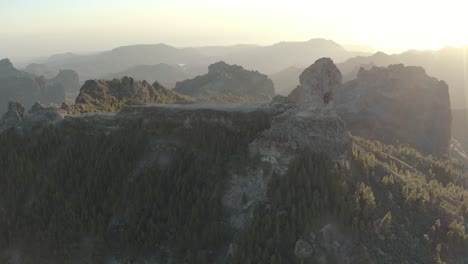 Beautiful-drone-shot-at-golden-hour-with-lens-flare-of-a-mountain-panorama-with-forest-of-roque-nublo,-gran-canaria