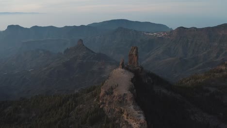 Vuelo-De-Drones-De-Una-Gran-Roca-En-La-Cima-De-Una-Montaña-A-La-Hora-Azul-Con,-Panorama-De-Montaña,-Roque-Nublo,-Pico-De-Las-Nieves,-Gran-Canaria