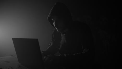 Computer-hacker-in-hoodie-with-laptop-in-dark-room