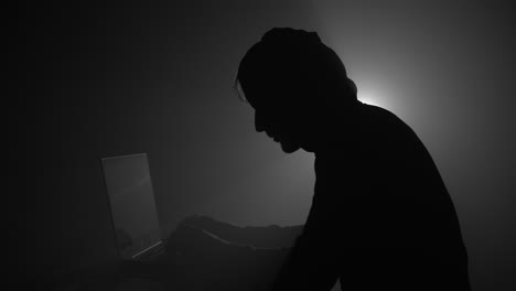 Silhouette-of-computer-hacker-in-hoodie-with-laptop-in-dark