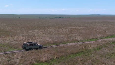 Circling-drone-shot-of-off-road-vehicle-drives-through-grasslands-in-Serengeti