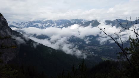 Scenic-german-high-alpine-view-down-into-the-valley-with-a-cable-car-passing-trough-from-left-to-right,-bringing-tourists-back-into-the-valley,-many-clouds-in-the-background