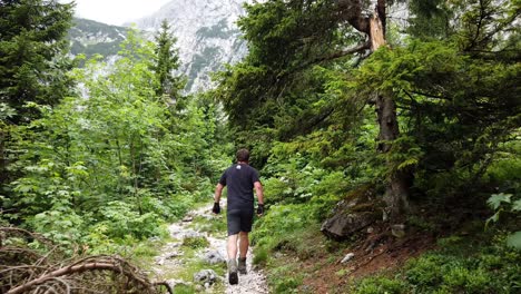 Following-a-hiker-in-black-shirt-walking-on-a-german-alpine-mountain-trail-with-trees-and-grass-and-a-high-peak-which-is-covered-in-clouds-and-fog